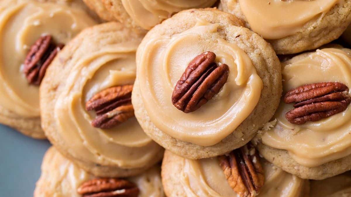 A close-up of several cookies topped with beige icing and a single pecan half on each.