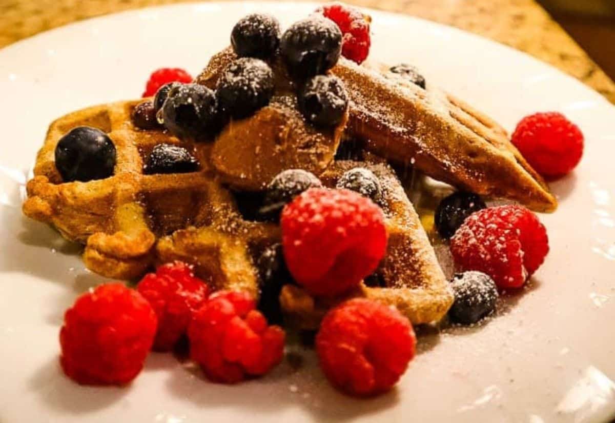 Waffles on a plate with fresh berries and powdered sugar.