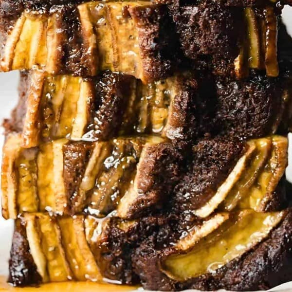 A close-up view of a moist, decadent chocolate banana bread. The bread is richly textured with chunks of chocolate and slices of banana throughout. A shiny glaze coats the top, highlighting its delicious, caramelized surface. Perfect for those exploring banana bread recipes. A knife's handle is visible to the side.
