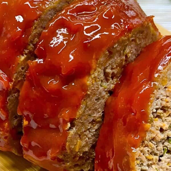 Sliced meatloaf topped with a glossy layer of ketchup, displayed on a wooden cutting board.