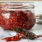 A partially opened jar of fig jam with seeds visible, accompanied by a spoon with some jam on it.