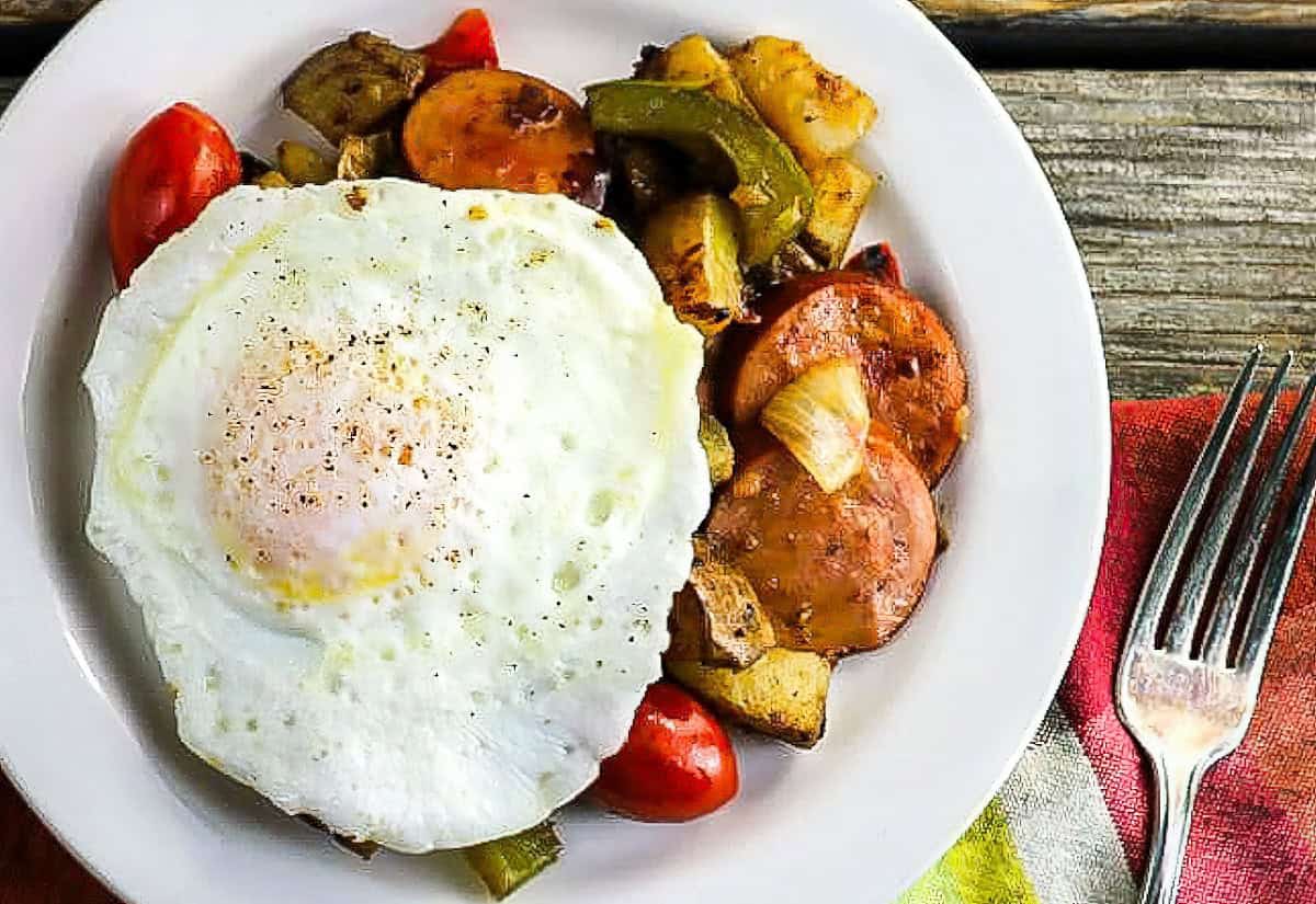 A fried egg on top of smoked sausage hash.
