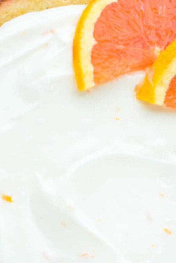 A round cake with white icing garnished with orange slices.