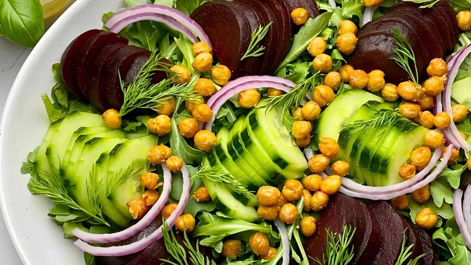 The image shows beet slices, cucumber slices, red onion rings, chickpeas, arugula, and dill on a white plate.