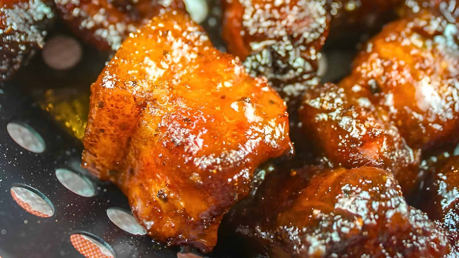 Glazed, caramelized pork belly pieces in a perforated pan.
