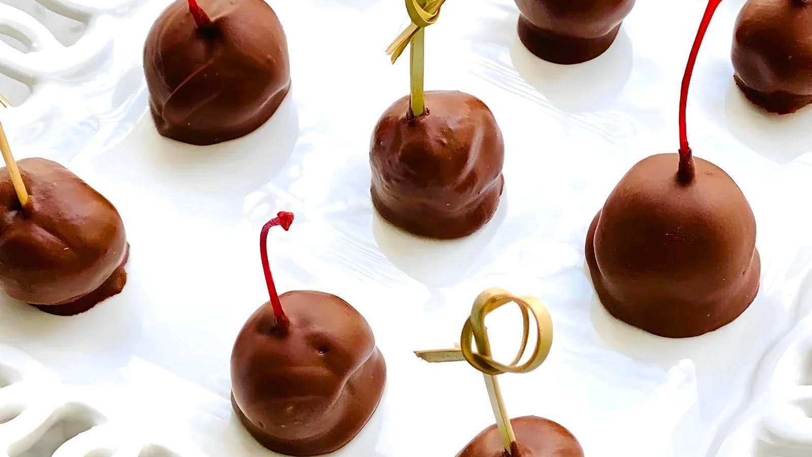 Chocolate-covered cherries with decorative toothpicks on a white plate.