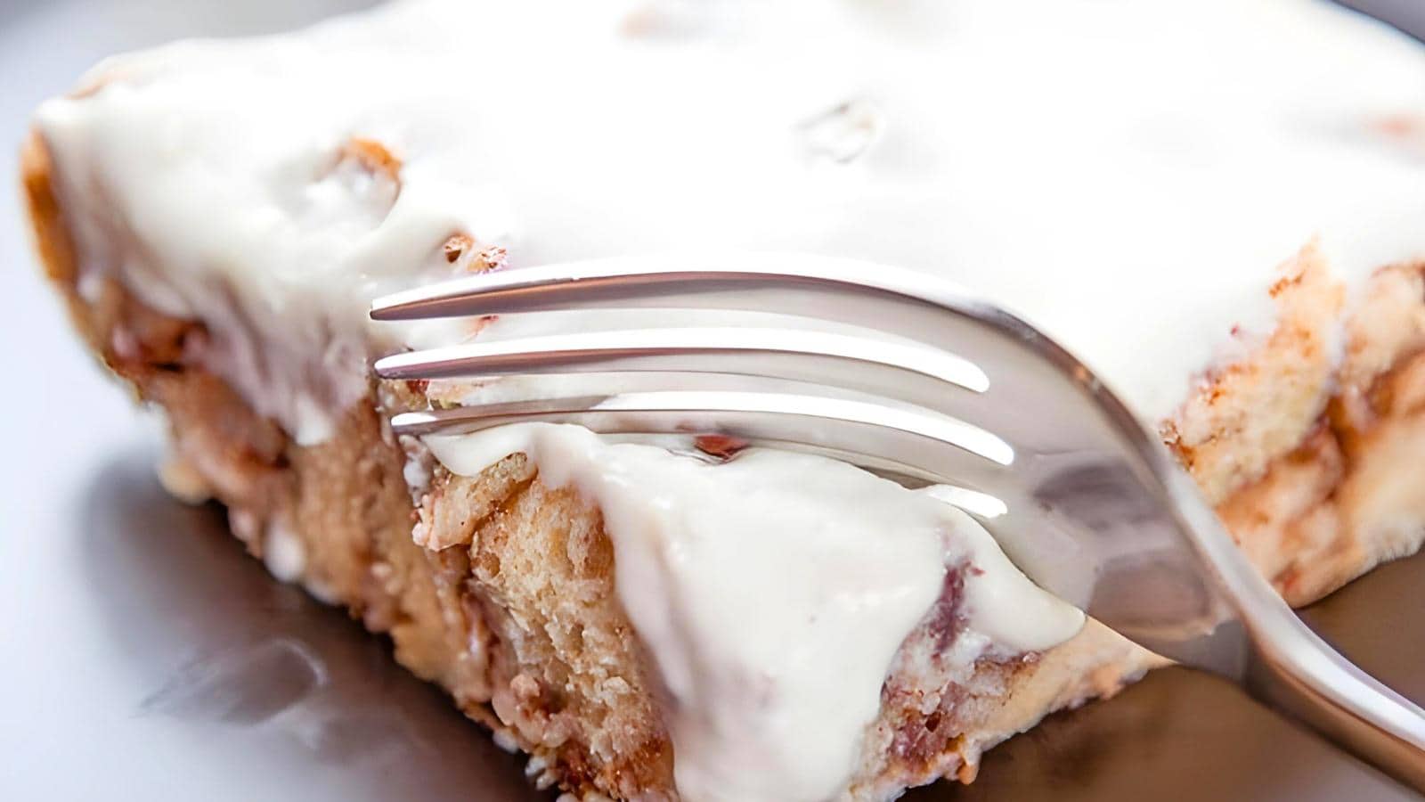 A fork cutting into a cinnamon toast topped with white icing.