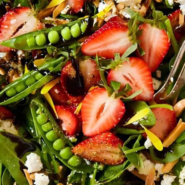 Fresh spinach, sliced strawberries, snap peas, crumbled cheese, light vinaigrette dressing, partially visible fork.
