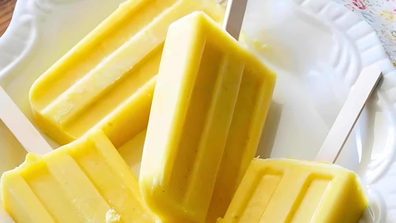 Four yellow popsicles on a white plate.