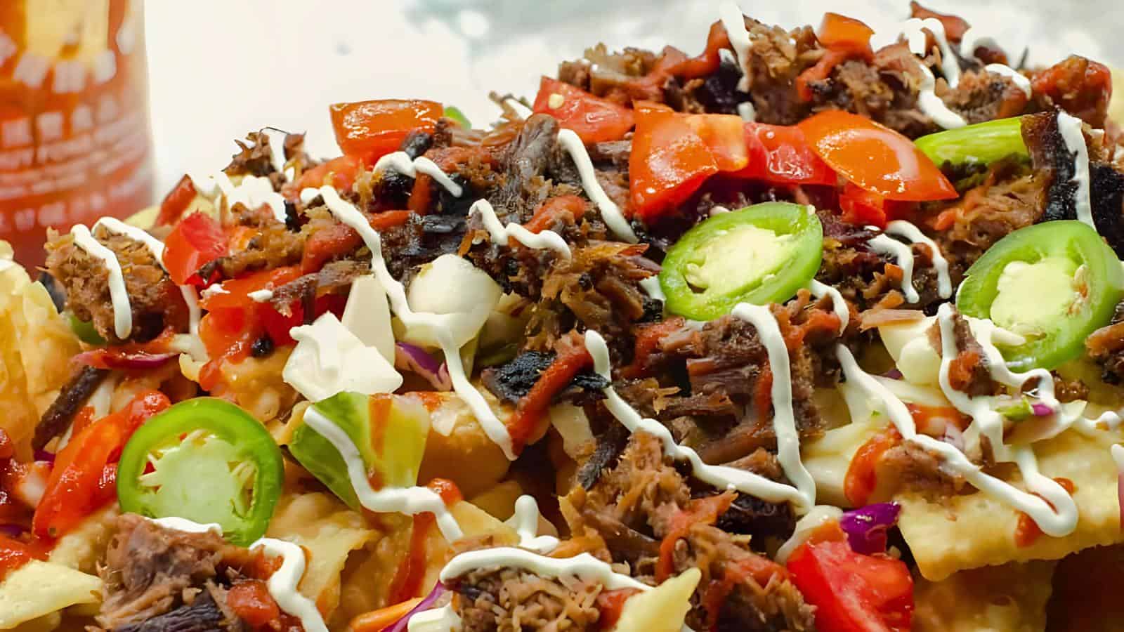 Nachos topped with shredded meat, sour cream, diced tomatoes, jalapeño slices, and melted cheese.