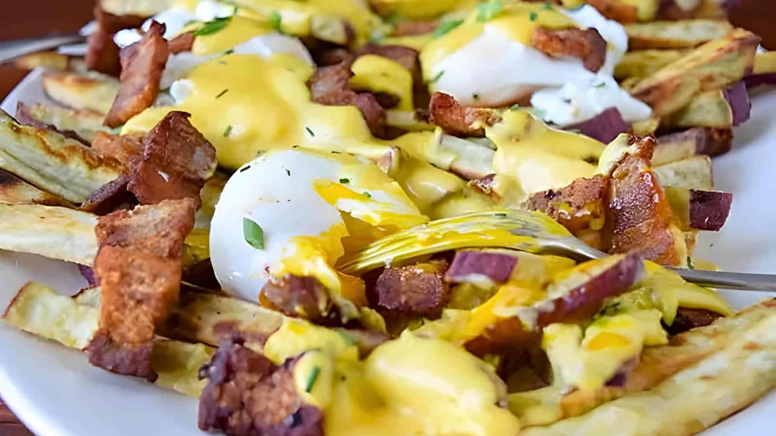 A dish of loaded fries with a creamy yellow sauce, poached eggs, bacon pieces, and garnished with herbs.