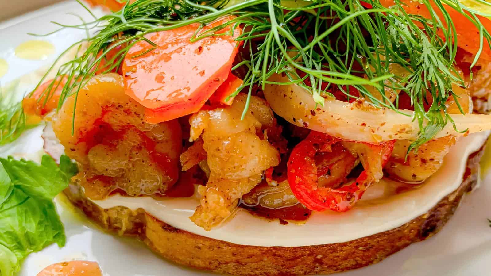 Open-faced sandwich topped with bacon strips, tomato slices, fresh dill, and mayonnaise on a slice of bread, with lettuce on the side.