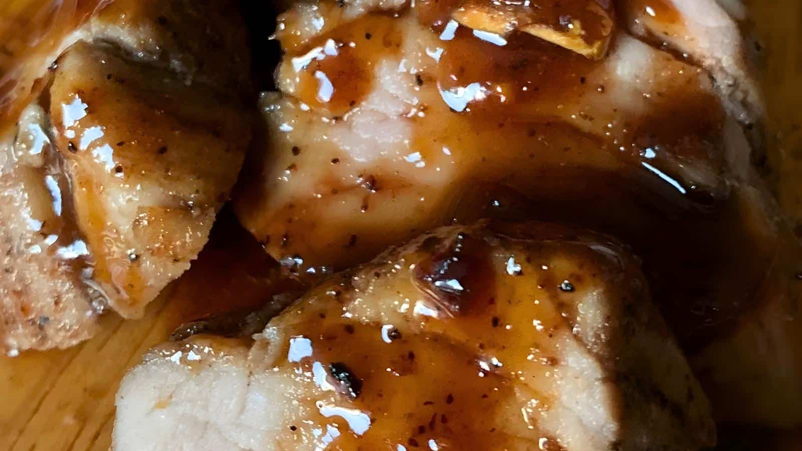 Cooked meat slices covered in a glossy, brown sauce on a wooden surface.