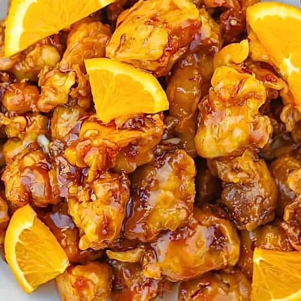 A bowl of crispy fried chicken pieces in a glossy orange sauce, garnished with fresh orange slices.