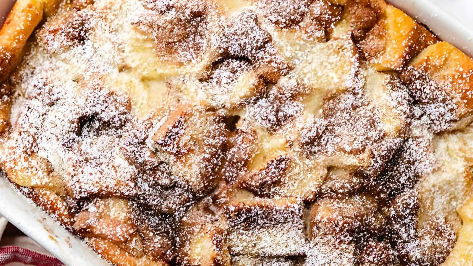 A white rectangular dish with baked bread pudding topped with powdered sugar.
