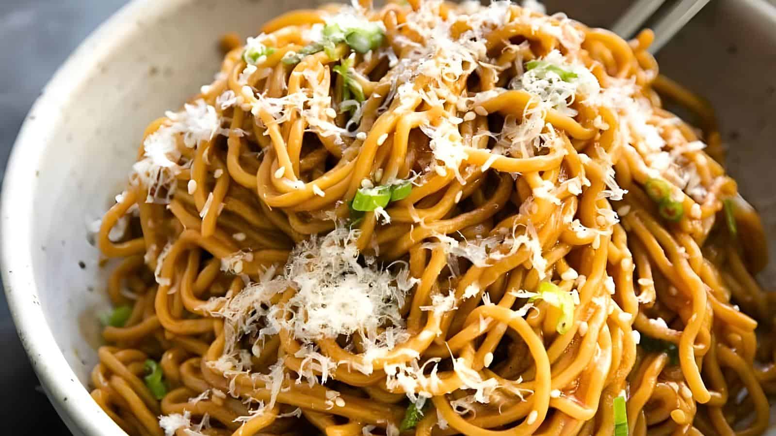 A bowl of spaghetti noodles topped with grated cheese and garnished with green onions. The dish is presented in a light-colored bowl, and chopsticks are resting on the edge.