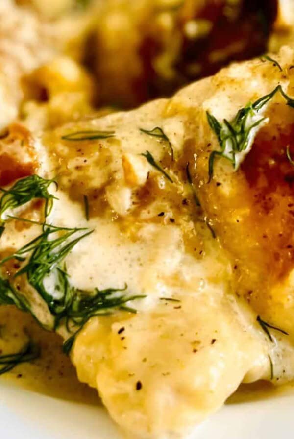 A plate of baked chicken topped with a creamy sauce and garnished with fresh dill.