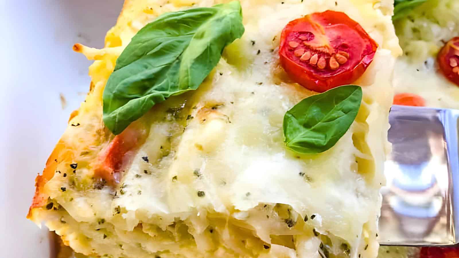 A close-up of hashbrown with melted cheese, spinach leaves, and cherry tomato slices on top.