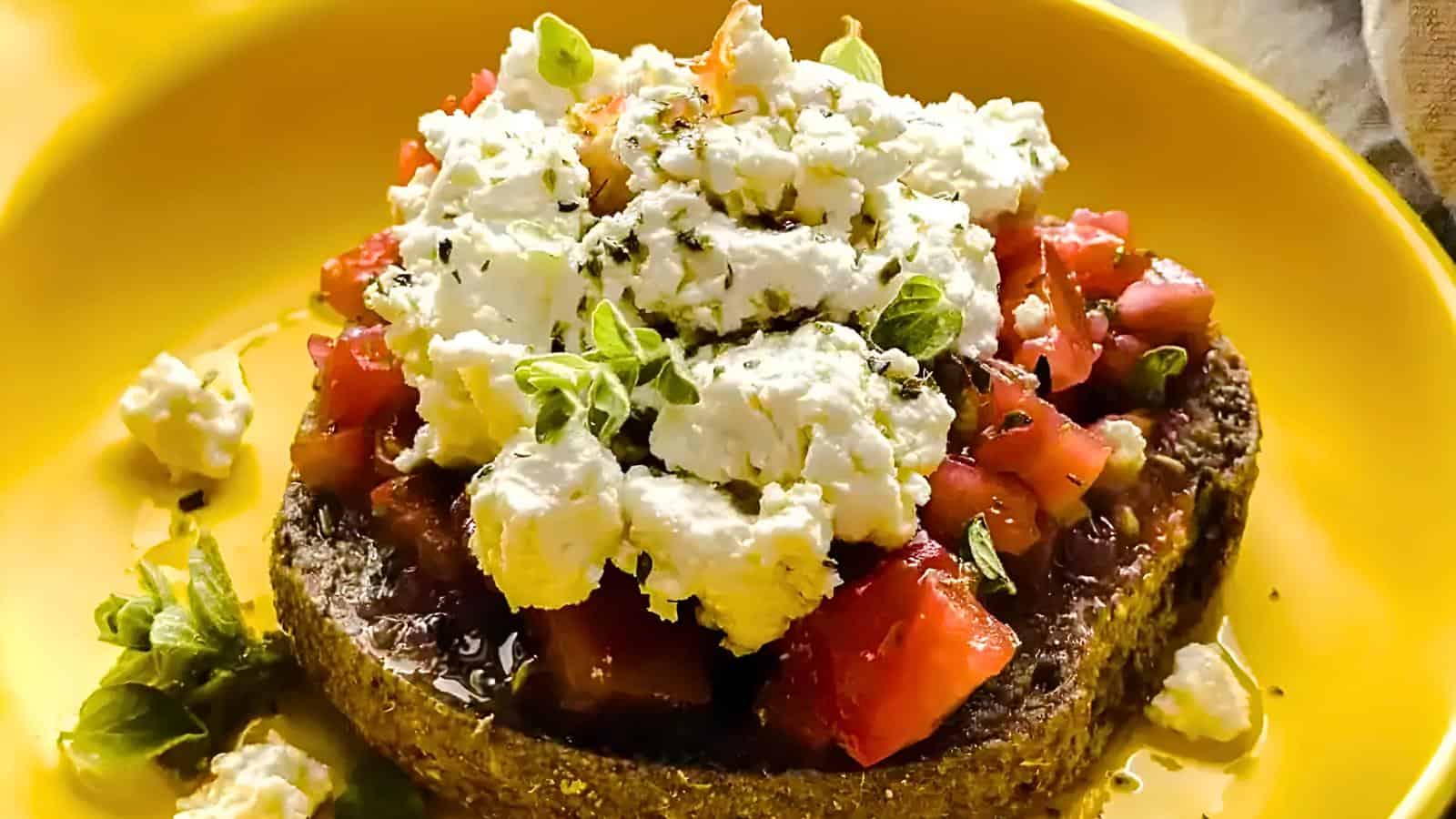 A slice of bread topped with diced tomatoes, crumbled feta cheese, and fresh herbs on a yellow plate.
