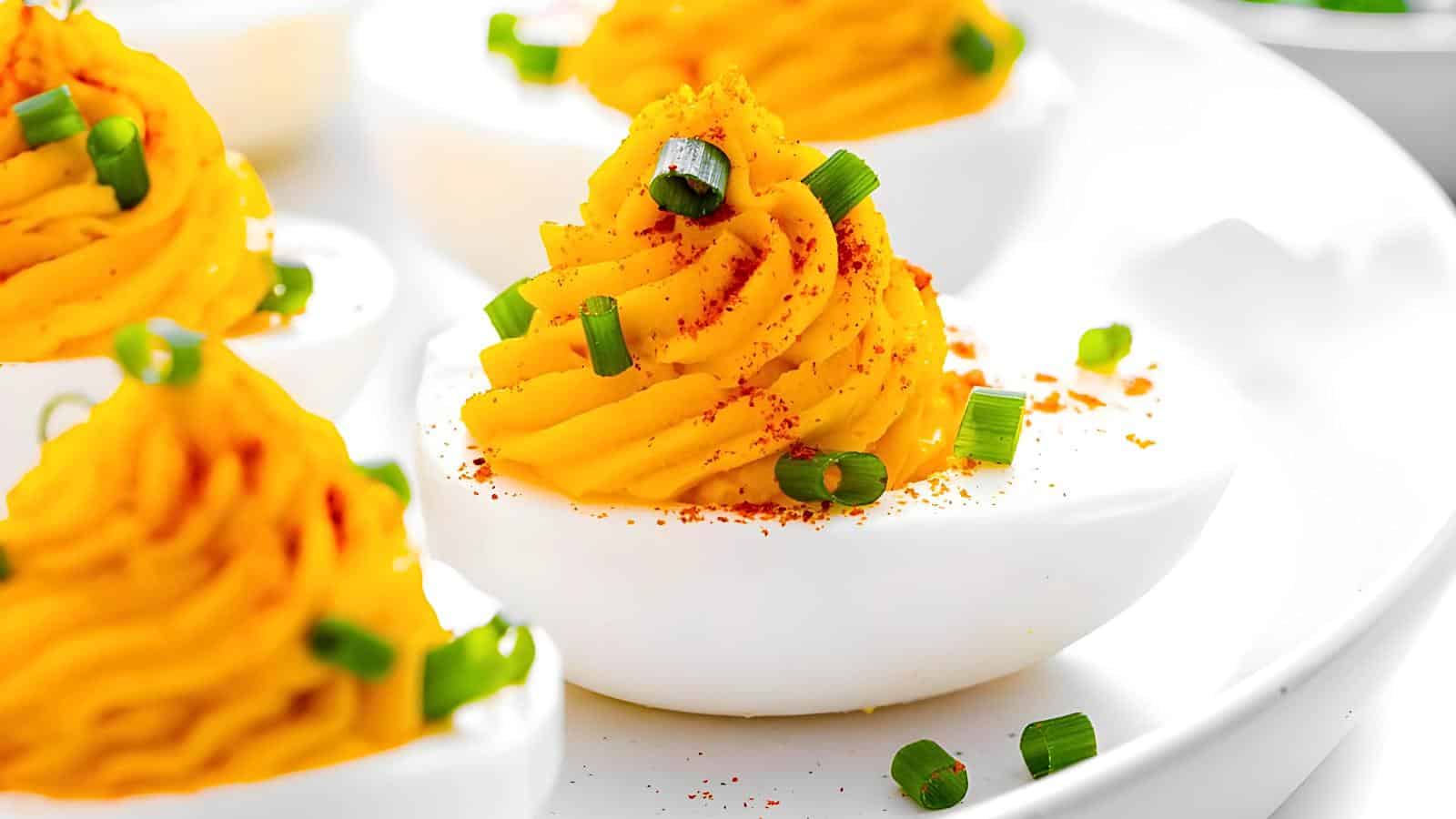 Deviled eggs garnished with chopped green onions and a sprinkle of paprika on a white plate.