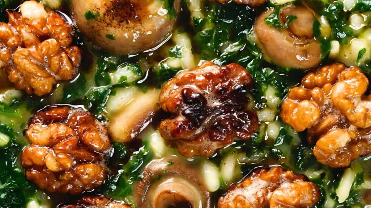 A close-up view of a delicious-looking dish featuring cooked walnuts, sliced mushrooms, and finely chopped greens in a savory sauce. The ingredients are well mixed, creating a colorful and appetizing texture.