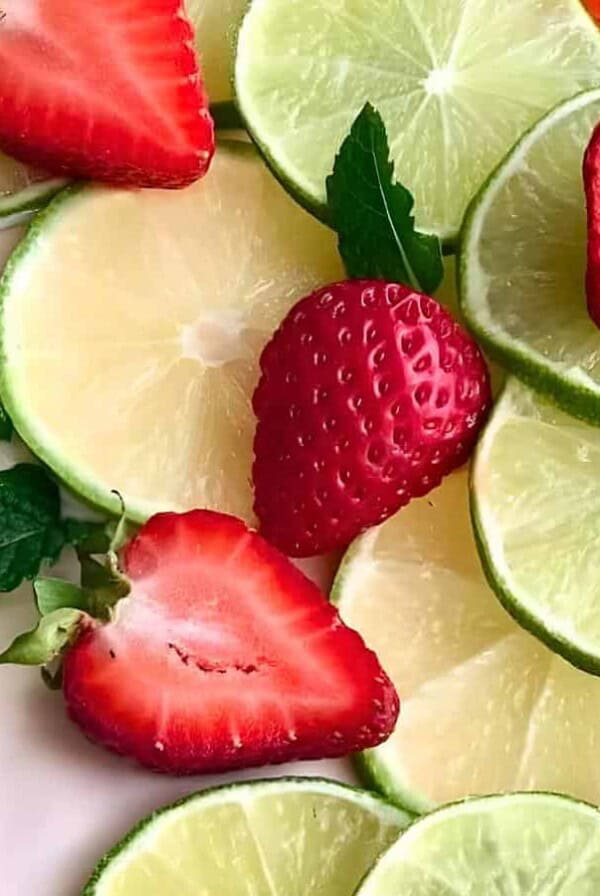 A slice of pie with a creamy pink filling and a graham cracker crust, topped with lime slices, strawberries, and mint leaves.