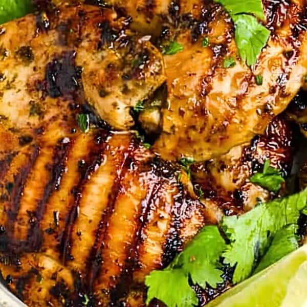 Grilled chicken thighs garnished with fresh cilantro and lime wedges.