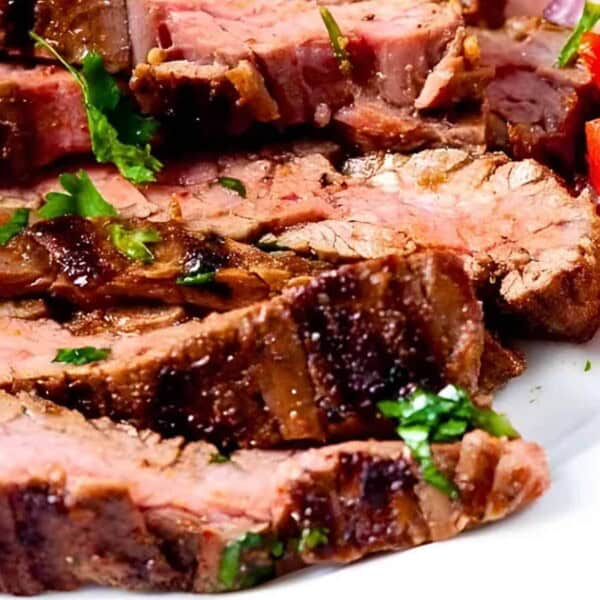 Sliced grilled steak garnished with fresh herbs, served with diced tomatoes and onions on a white plate.