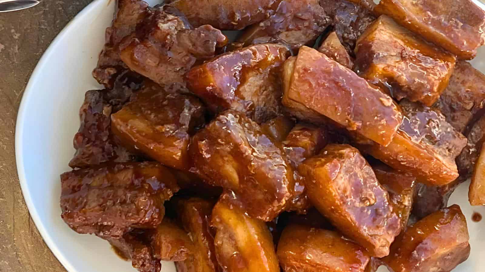 A pile of glazed short belly coated in a rich, brown sauce on a white plate.