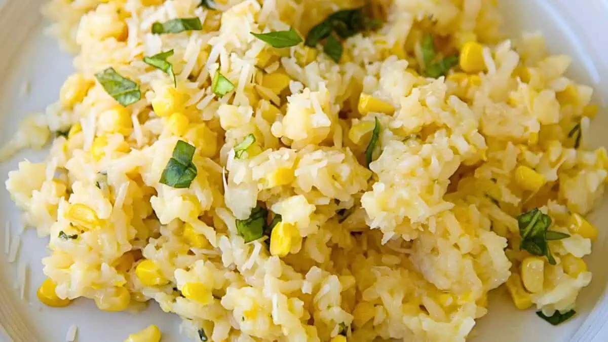 A close-up view of a plate filled with creamy risotto mixed with corn kernels and garnished with chopped fresh basil leaves. The dish is light yellow in color with vibrant green specks from the basil.