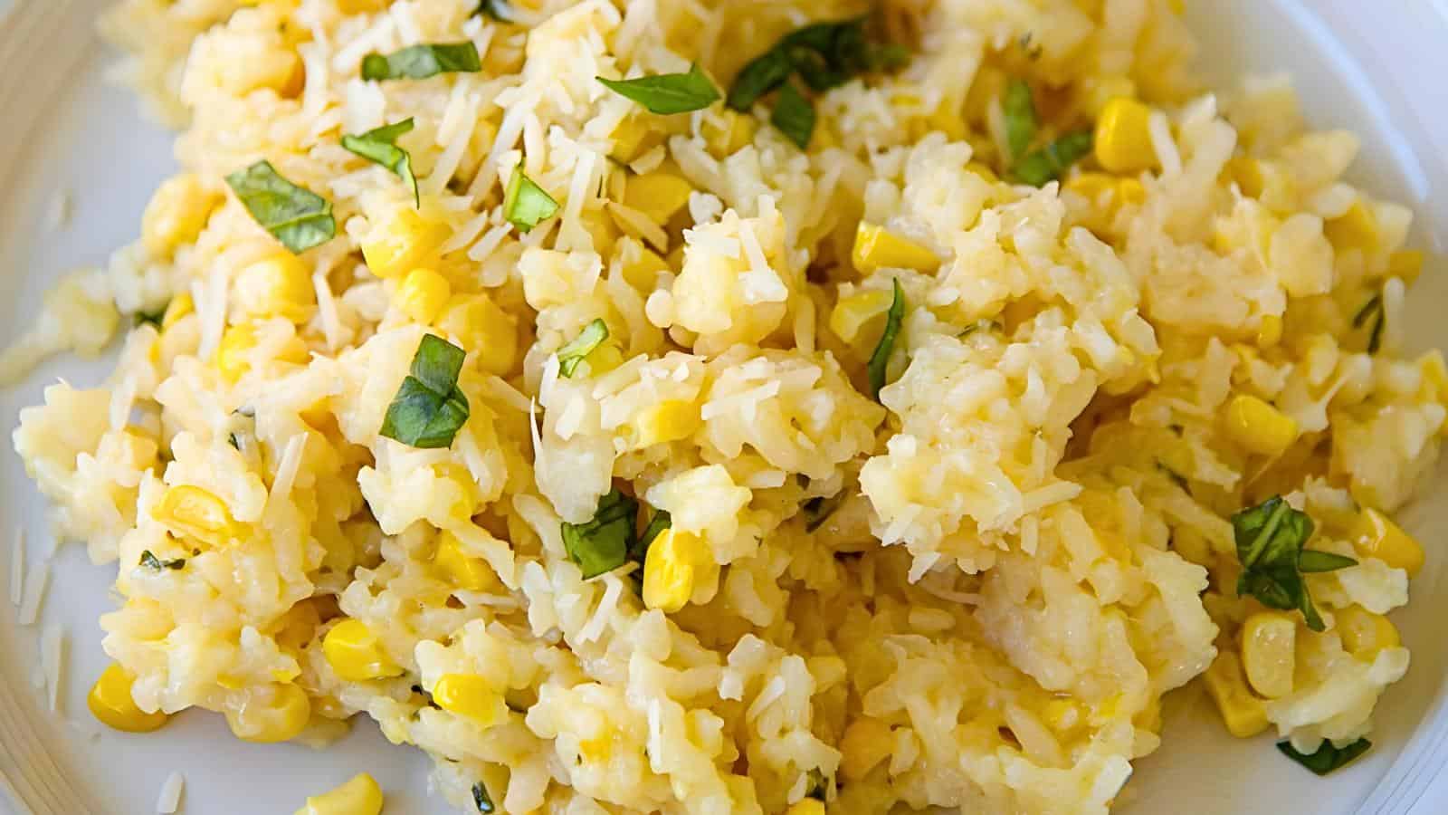 A close-up of a plate containing rice, corn, shredded cheese, chopped green herbs, all mixed in a creamy texture.