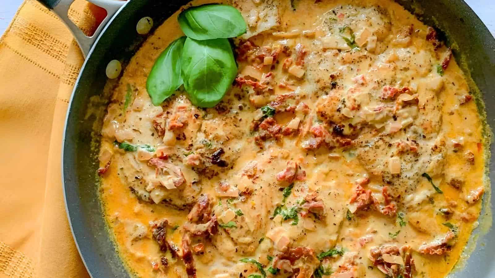 A skillet with creamy chicken, garnished with fresh basil leaves.