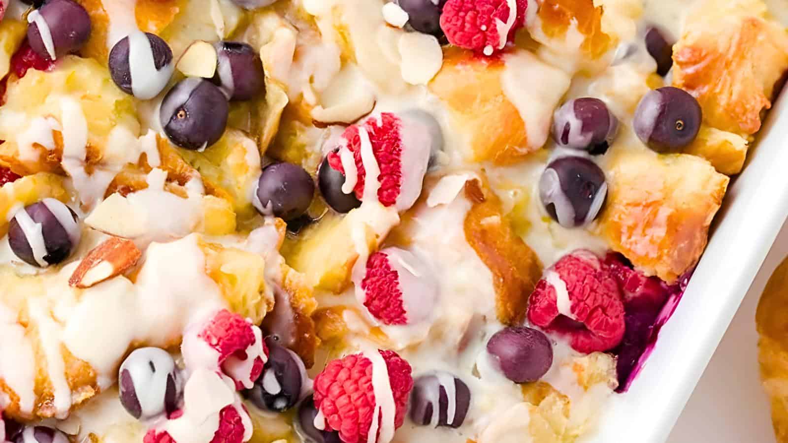 A croissant with raspberries, blueberries, almond slices, and white icing drizzle.