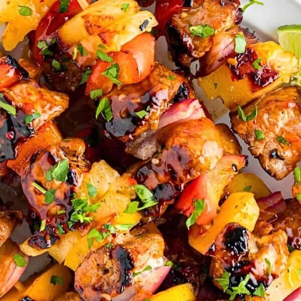 Grilled meat and vegetable skewers garnished with chopped herbs are arranged on a white plate with lime wedges.