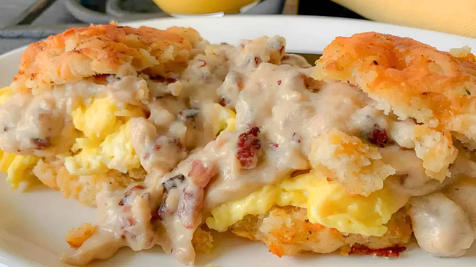 A biscuit sandwich filled with scrambled eggs and topped with sausage gravy on a white plate.