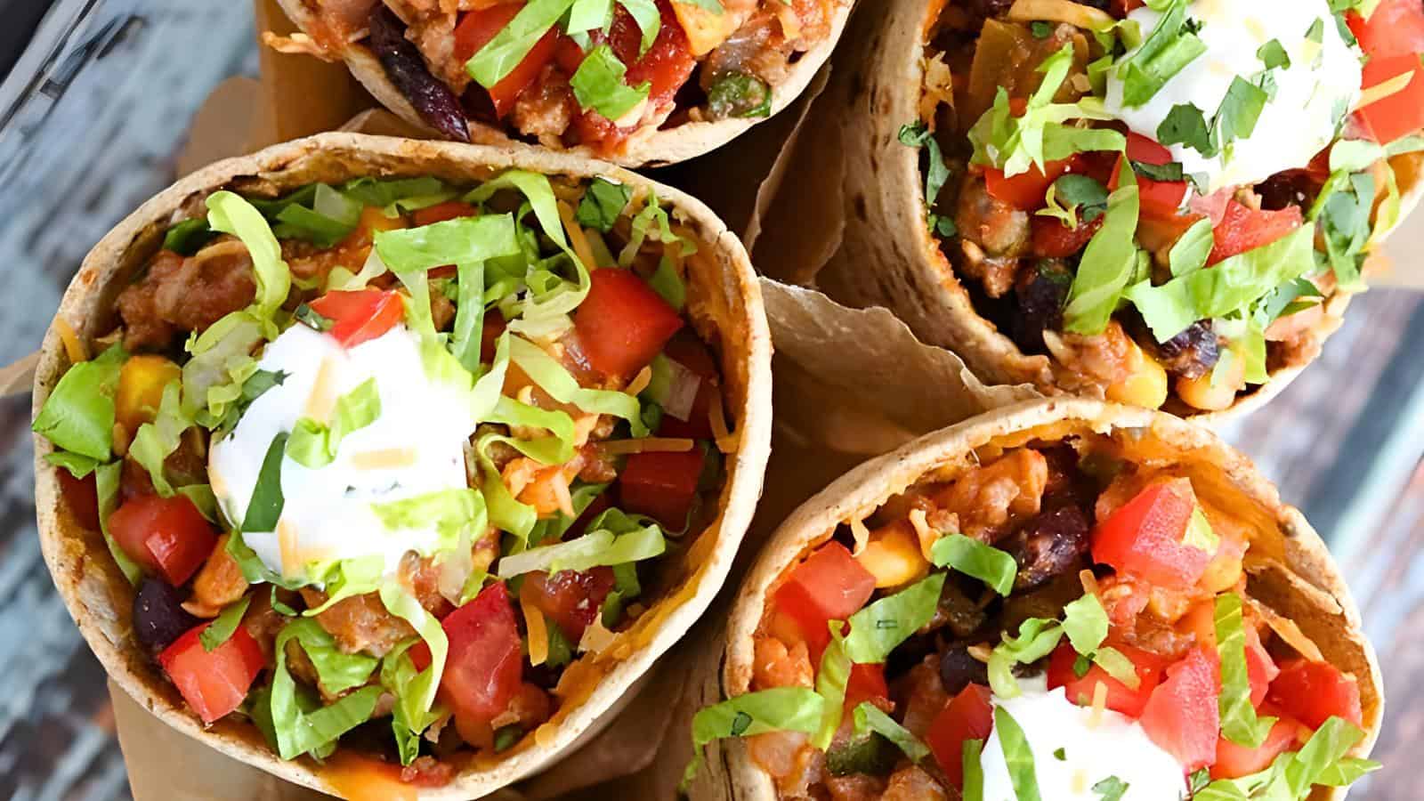 Four taco cones with diced tomatoes, shredded lettuce, sour cream, beans, rice, and chopped cilantro.