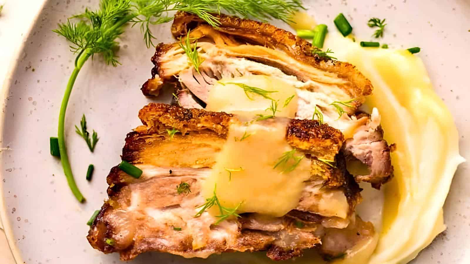 Close-up of a plated dish with two slices of roasted pork topped with a creamy sauce, garnished with fresh dill and chives, alongside pureed vegetables.