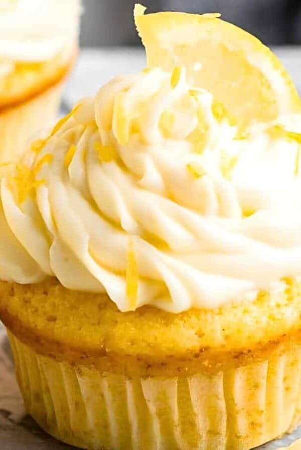 A close-up of lemon cupcakes with creamy frosting and small lemon wedges on top, set on a marble surface.