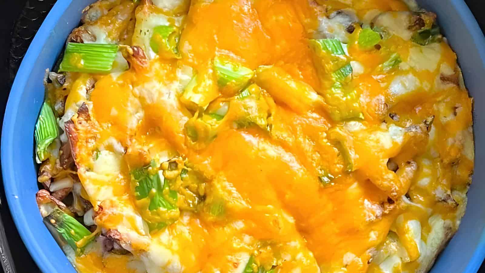 A baked dish topped with melted cheese and chopped green vegetables in a blue baking dish.