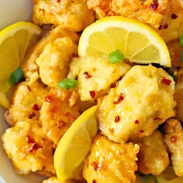 A bowl filled with crispy fried chicken pieces, garnished with lemon wedges and chopped green onions. The chicken is lightly coated in a golden batter.