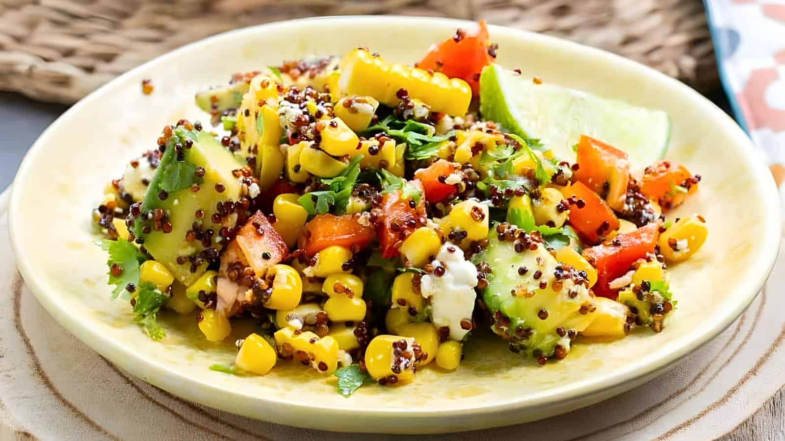A plate of quinoa salad with corn, diced tomatoes, avocado, chopped cilantro, and a lime wedge.
