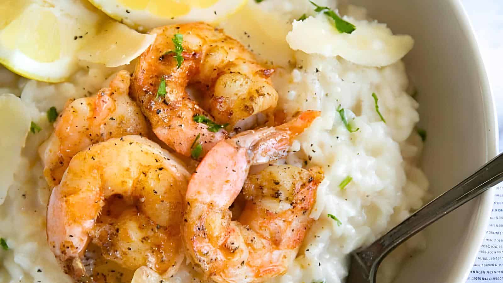 Shrimp on a bed of creamy risotto, garnished with lemon slices and herbs. A fork is partially visible to the right.