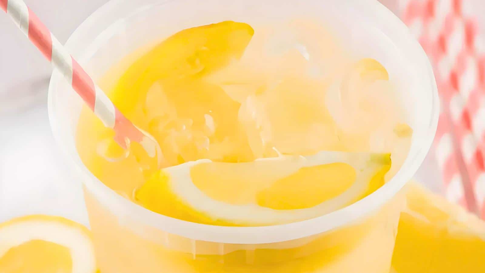 A plastic cup with lemonade, lemon slices, and a red-and-white striped straw.