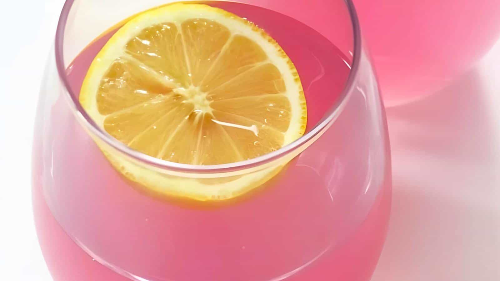 A glass of pink drink with a lemon slice on top.