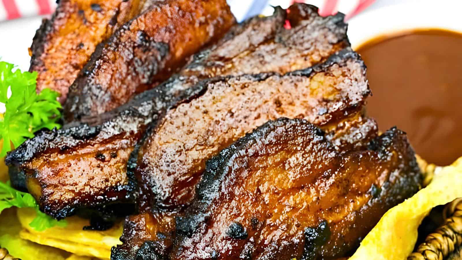 Grilled BBQ belly with a charred exterior, garnished with parsley, accompanied by a bowl of barbecue sauce.