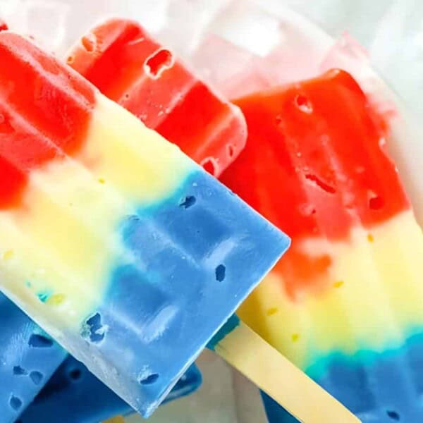 Colorful popsicles with red, yellow, and blue layers on sticks, placed on a light background with striped straws.