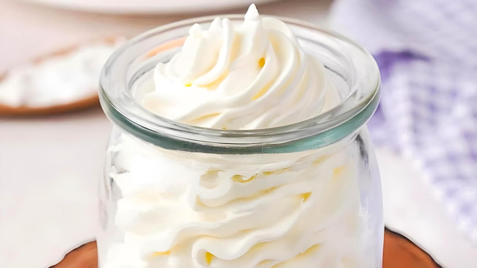 A glass jar filled with swirled, whipped cream, a checkered cloth, and a wooden spoon.