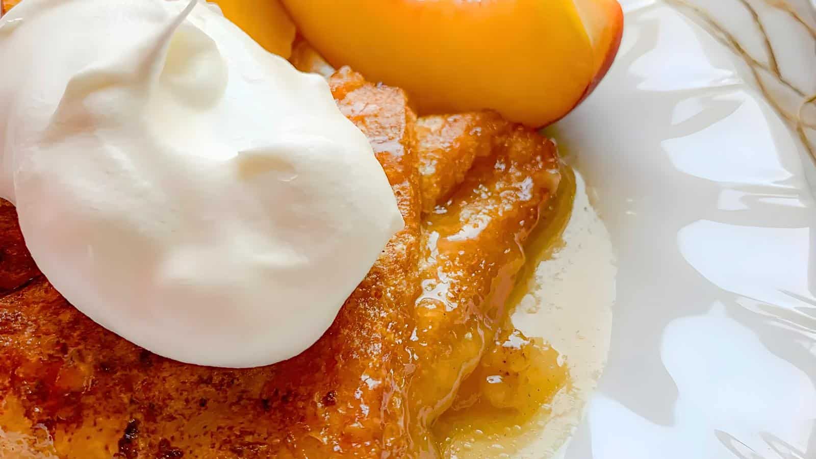 A slice of dessert topped with whipped cream, accompanied by sliced peaches, all in a white dish.