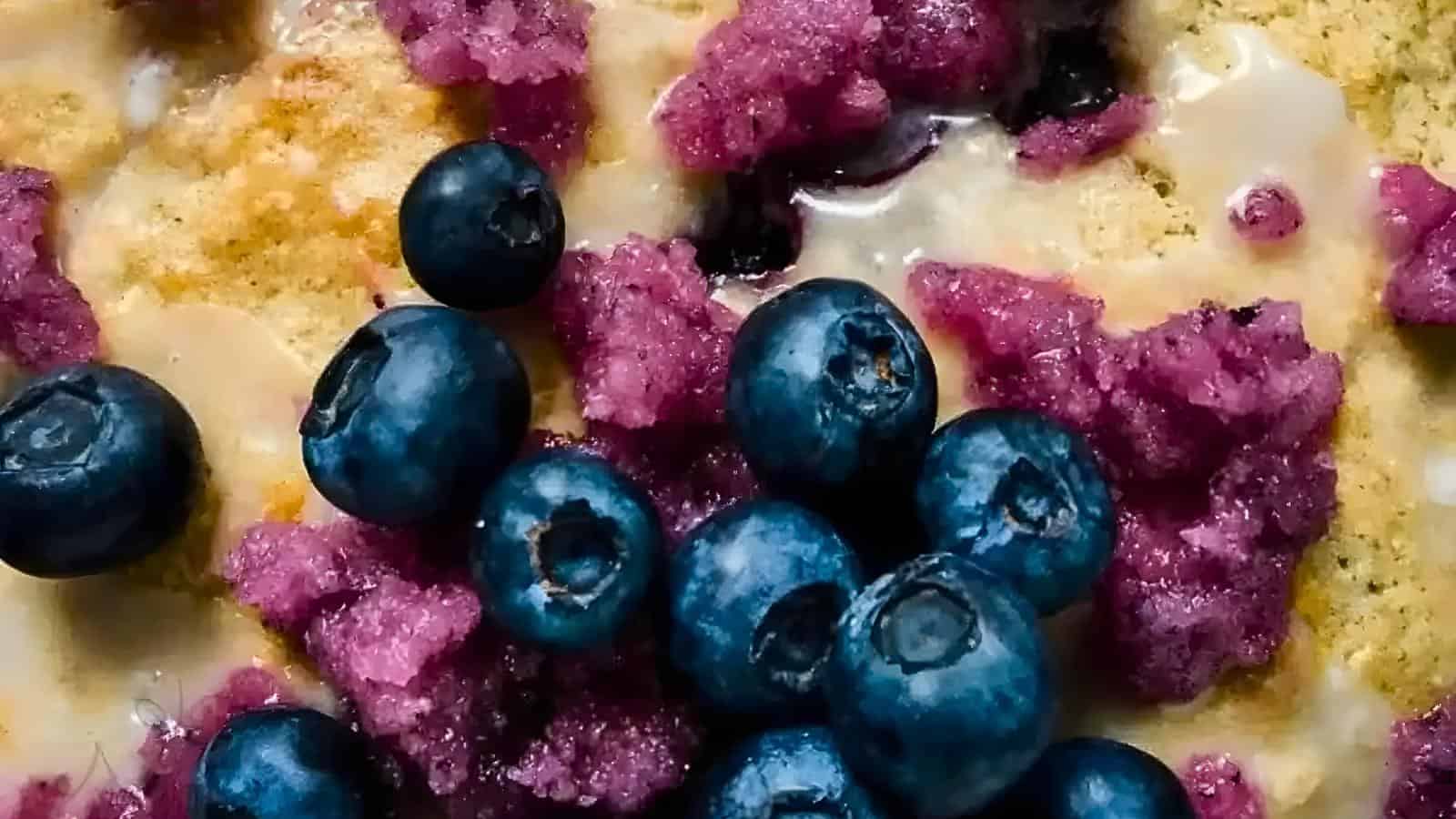 A dish with blueberries and a purple crumbly topping, garnished with a drizzle of sauce.