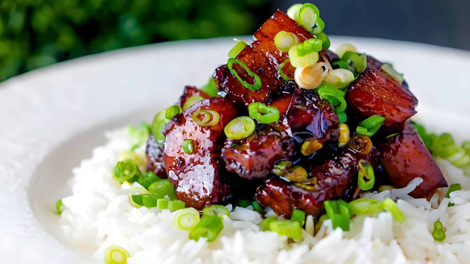 A plate of white rice topped with glazed caramelized pork, garnished with chopped green onions.